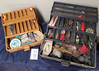 Two vintage fishing tackle boxes, one brown and one gray, open to show compartments with fishing lures, line, and accessories