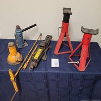 Full view of two bottle jacks, one scissor jack, two jack stands, and a car jack handle on a blue cloth surface.