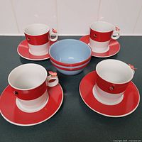 Full view of the tea party set consisting of 4 red and white teacups and saucers along with a blue and red striped snack bowl.