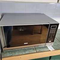 Front and side view of microwave oven showing its silver and black color with mirrored front door and reflective surface.