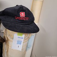Rolled nautical charts bundled with rubber bands, some labels visible with maritime navigation details, alongside a black Seaspan captain cap on top.