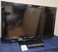 Front view of the Panasonic flat-screen TV, showing the screen and the base stand, placed on a blue cloth surface.