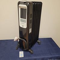 Full view of black Noma digital oil-filled portable radiator heater with control panel and caster wheels.