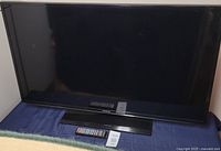 Full front view of Samsung 48-inch flat screen TV on a blue surface with remote and tag in front.