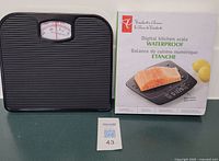 Photo of black mechanical bathroom scale with analog dial, and the boxed digital waterproof kitchen scale with salmon fillet image on box.