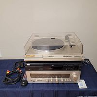 Full shot of the stereo lot on a navy cloth. The Garrard turntable sits on top, below it an RCA DVD player, with the ICC Electronics stereo receiver at the base. Cables and remote included on the side.