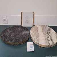 Two round marble hot pads/trivets side by side on a kitchen counter, one dark gray and one light beige, both solid pieces with polished tops.