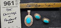 925 silver earrings and pendant set placed next to a ruler for scale, showing turquoise stones and hammered silver texture.