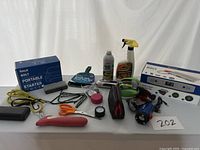 Overall view of the lot showing all items on a white surface including a boxed Halo Bolt Ultimate Portable Jump Starter and various tools and car cleaning products