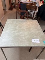 Folding card table with beige textured surface, showing general condition and table surface