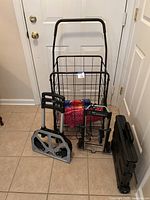 Full view photo showing all three carts standing on a tiled floor in front of a white door, including the foldable hand truck, rolling shopping cart with fabric bag, and smaller collapsible cart.