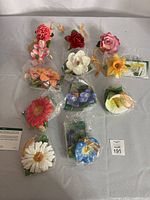 Complete view of 10 ceramic flower ornaments sealed in plastic, displayed on table.