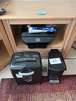 Wide shot showing Bonsaii paper shredder, small black lidded trashcan with foot pedal, and HP Envy printer in open desk shelf.