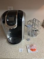 Keurig coffee maker with pod holder, measuring cup, and razor tool on countertop