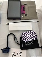 Amazon Kindle Fire tablet displayed on purple and gray protective case alongside stylus in box, USB charging cable, and Halo accessory pouch.