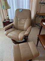 Full view of tan leather reclining chair with matching ottoman on wood bases