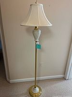 Full view of the tall floor lamp showing brass-colored base and ceramic detailing with white fabric shade.