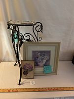 Full view of plant stand with tile top beside two framed floral artworks on white background with ruler for scale.