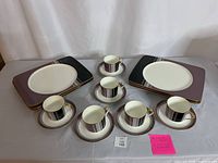 Set of six rectangular plates, four cups, and four saucers displayed on a table illustrating the design pattern and quantity.