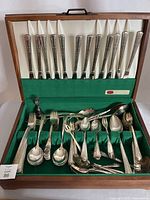 Full set of silverware pieces arranged inside felt-lined wooden storage box, showing multiple forks, spoons, and knives.