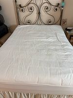Full view of bed with white mattress pad on metal headboard and bed skirt