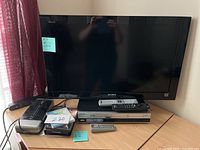 Front view of the TV, DVD/VHS player, and remotes on wooden desk.