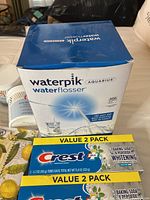 Photo of Waterpik Aquarius Water Flosser box and Crest toothpaste value 2 pack boxes, showing product branding and packaging condition.