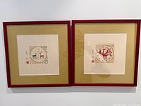 Frontal view of two artist proof prints side by side in red frames with tan mats, showing stylized animal motifs and artist signature with AP notation.
