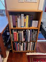 Front view of the light wood finish bookshelf filled with books (books not included in sale).