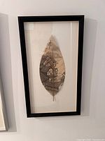 Framed leaf painting showing a landscape scene with buildings and mountains seen from the front