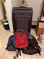 Photo of large suitcase standing upright with two backpacks in front, showing colors and general condition.