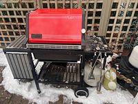 Weber Platinum Series propane BBQ showing the red lid, thermometer, burners, black metal frame, side shelves with some wear, propane tank attached, and technical controls on the side.
