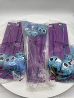 Three packages of cat wand toys with purple wands and attached blue fish plush toys in clear plastic wrapping on a white circular table.