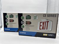Photo of two boxed Compass CE Series LED Emergency Exit Signs showing packaging design with product images and features including LED, 2 hour runtime, and dual face exit signs.