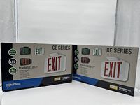 Two Hubbell CE Series LED Emergency Exit Signs in their original retail packaging showing product branding, LED illumination, and emergency features.
