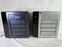 Two Promise Technology Inc. Pegasus2 R4 RAID storage systems shown side by side, one silver and one dark gray/black, both with four drive bays and Promise branding.