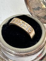 Angled top view inside metal and velvet case showing two rows of pave-set diamonds on gold band