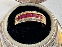 Top view of 14K gold band with five channel-set rubies and flanking diamond rows, displayed in a ring box.
