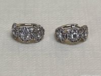 Front angle view of pair of 18K white gold huggie earrings on white background showing diamond clusters