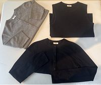Three knit pieces laid flat: grey cropped cardigan, black sleeveless top, black cropped cardigan