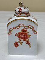 Frontal view of rectangular white porcelain scent bottle with red floral spray and gold-edged top