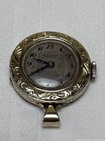 Front view of watch face showing silver-toned dial marked Rolex, black Arabic numerals, blued steel hands and ornate engraved bezel with bail