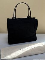 Front view of black nylon handbag on table with dust bag in foreground
