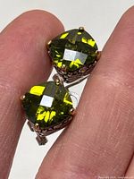 Close-up view of individual earring showing cushion cut green faceted stone and prong setting