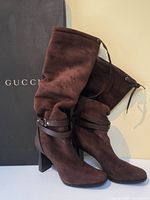 Front view of pair of brown suede boots with ruched shafts leaning against Gucci box