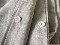 Close-up of two round light beige plastic buttons sewn on neutral linen fabric