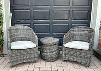 Two grey resin wicker chairs flanking round wicker table against garage door