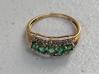 Front view of ring showing five round emeralds and diamond accents on band