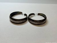 Pair of large sterling silver hoop earrings shown side by side with visible post backs and slight tarnish.