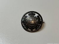 Front view of brooch on plain background showing coat of arms detail